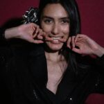 A woman playfully posing with a bow in her hair against a deep red background.